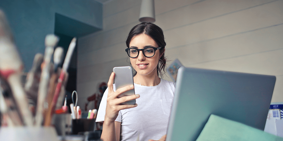 Kvinde med briller bestiller fra sin telefon ved sin computer
